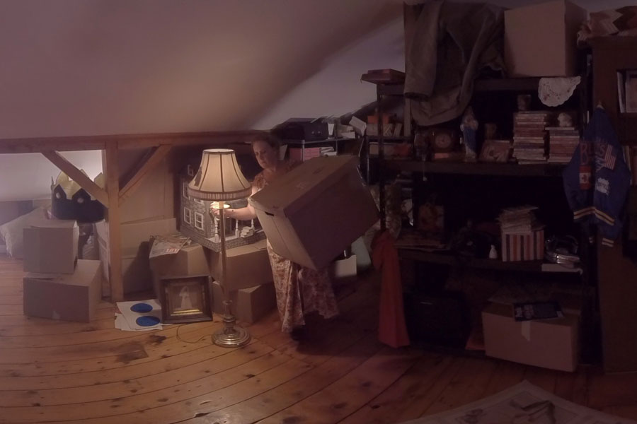 Dimly lit attic, mary-helen holds a box while turning the light on.